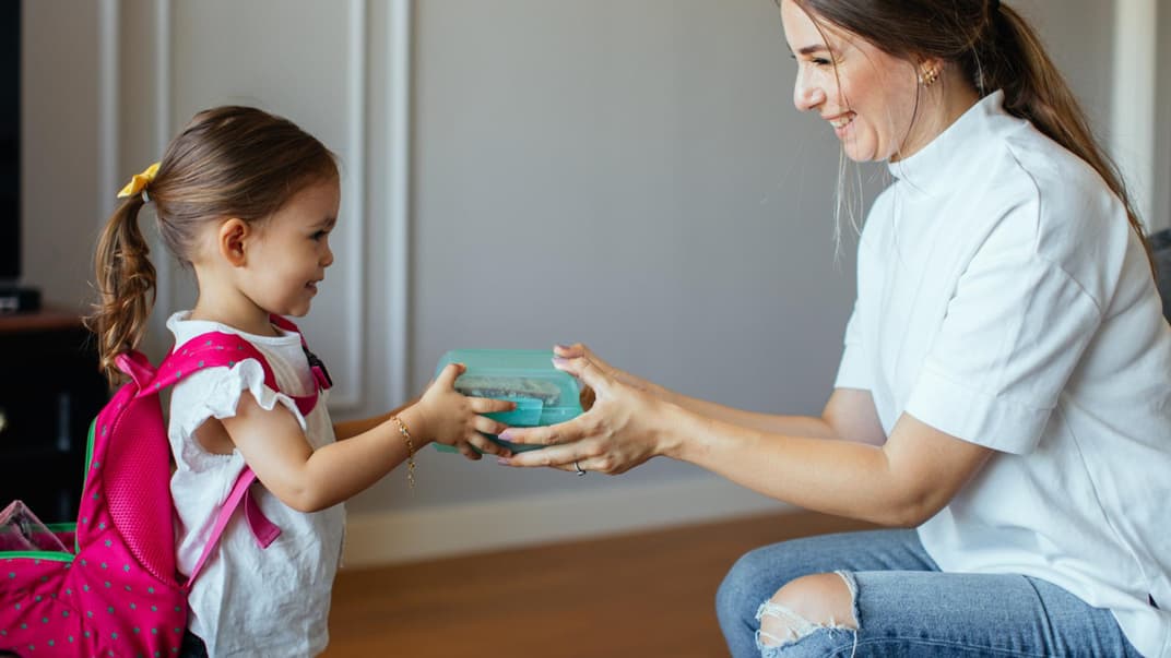 Mutter überreicht ihrem kleinen Kind eine Brotdose.