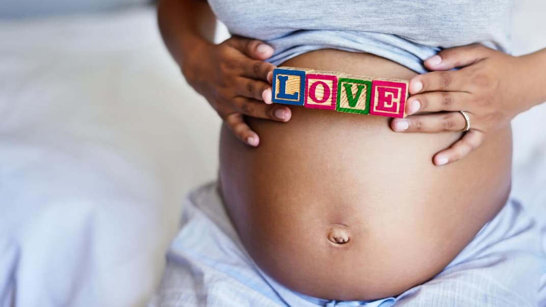 Eine Mama hält ein Love-Schild über ihren kugelrunden Babybauch. 