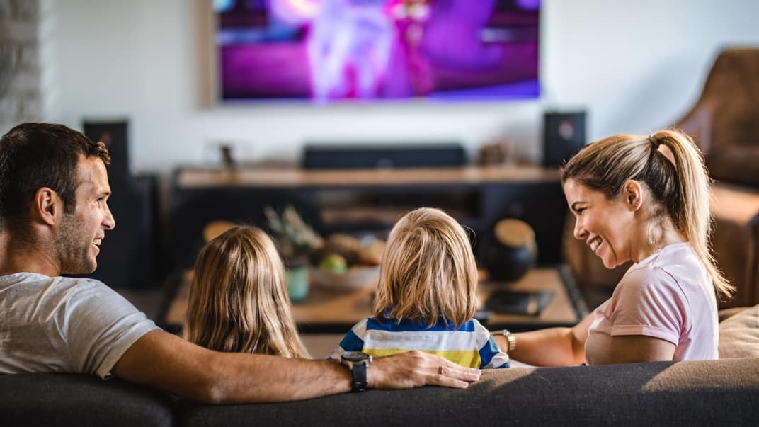 Mutter und Vater sitzen mit Sohn und Tochter auf dem Sofa vor dem Fernseher.