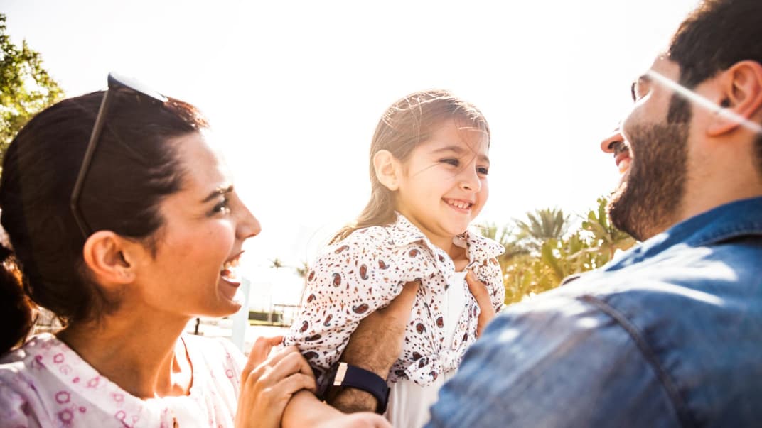 Mutter und Vater halten ihre lachende Tochter.