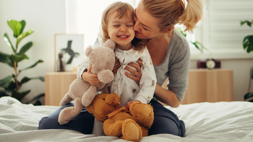 Mama umarmt Mädchen mit Kuscheltieren