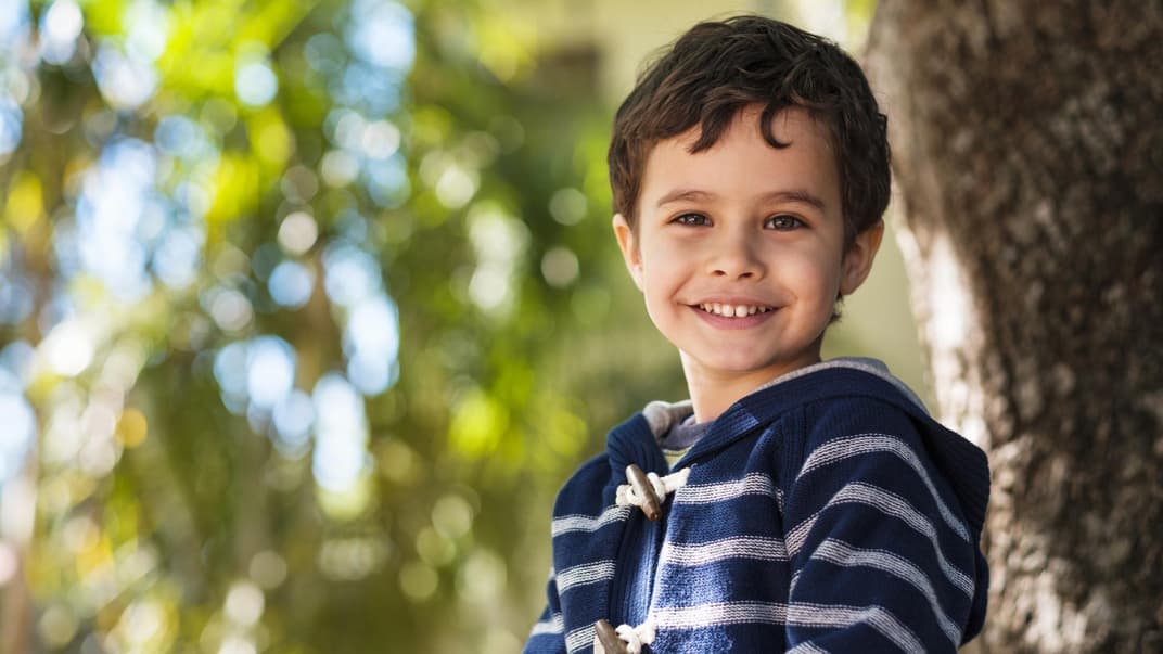 Ein dunkelhaariger Junge mit blau-weiß gestreiftem Pullover lächelt.