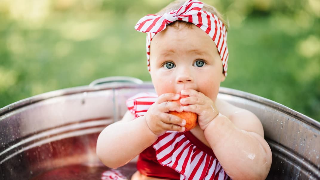 Ein Baby sitzt draußen in einer Badeschale.