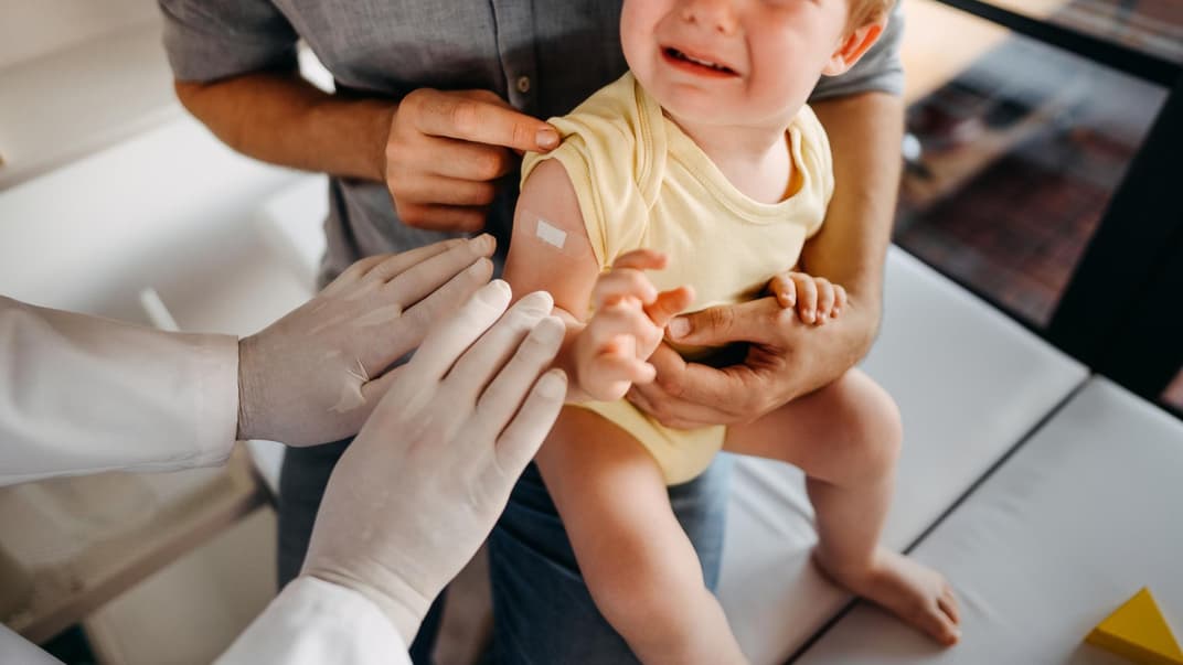 Ein Baby weint beim Kinderarzt und sitzt auf dem Schoß der Eltern