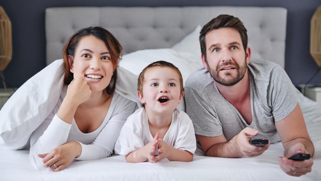 2-Jähriger guckt mit seinen Eltern einen Kinderfilm vom Bett aus