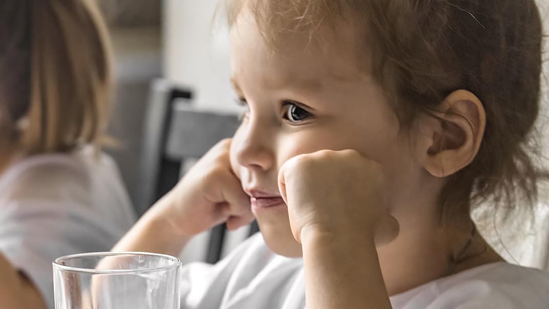Mädchen sitzt mit Ellenbogen aufgestützt am Tisch und sieht wütend aus