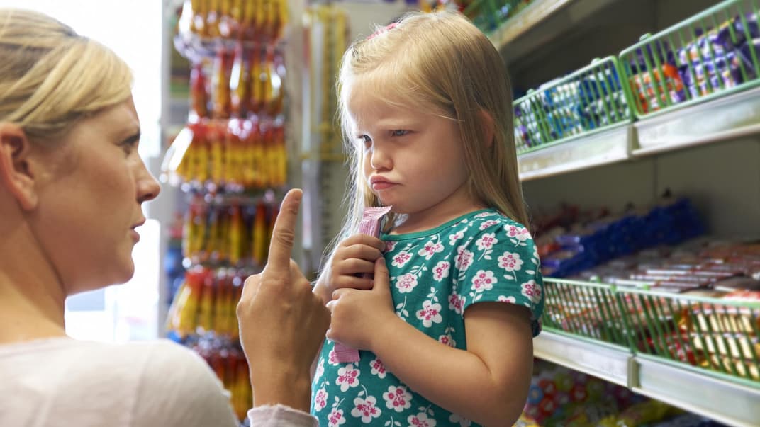 Mama schimpft mit ihrer Tochter, die im Supermarkt einen Riegel geholt hat 