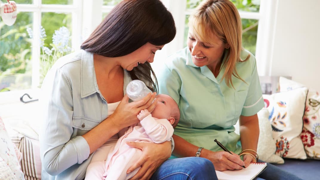 Mutter füttert ihr Baby, Mütterpflegerin sitzt daneben