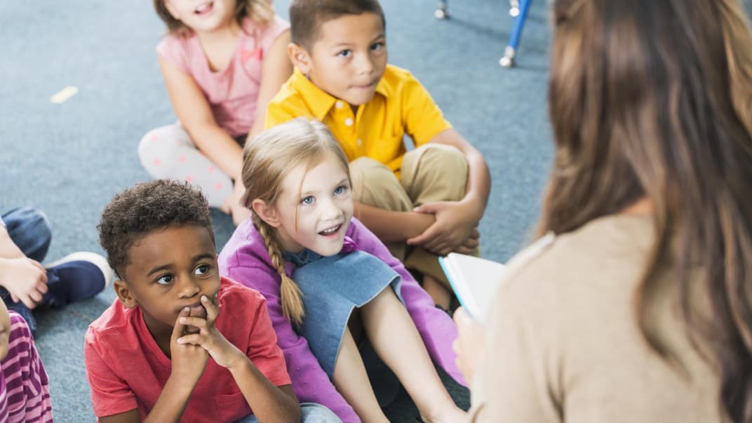 Kindergartenkinder hören einer Erzieherin beim Vorlesen zu