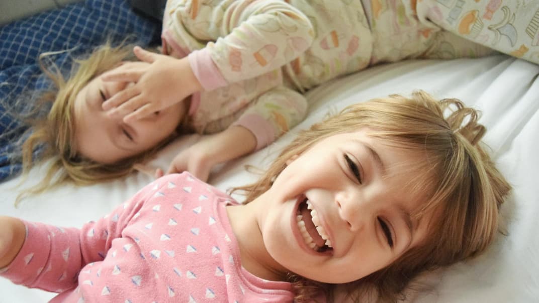 Zwei Kinder liegen lachend im Bett