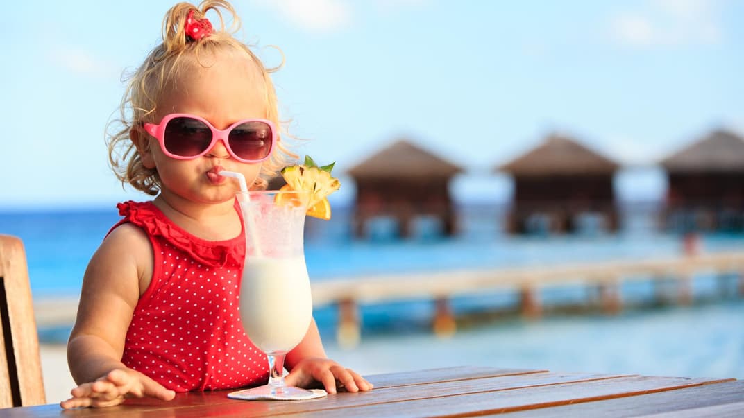 Ein kleines Mädchen mit rotem Badeanzug und Sonnenbrille trinkt einen Kinder-Cocktail.