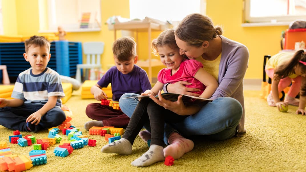 Erzieherin liest einem Vorschulmädchen ein Buch vor und beide lächeln