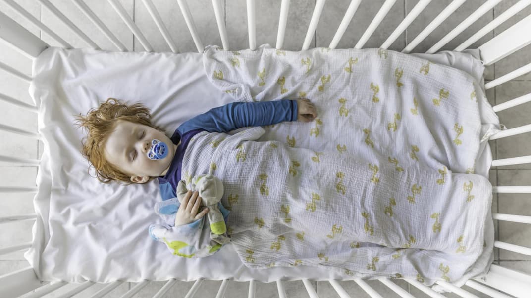 Rothaariges Kleinkind mit Schnuller liegt schlafend im Gitterbett