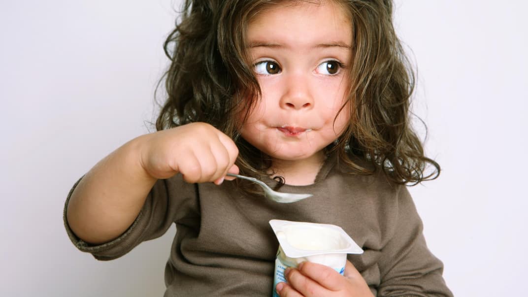 Kleinkind löffelt einen Joghurt.