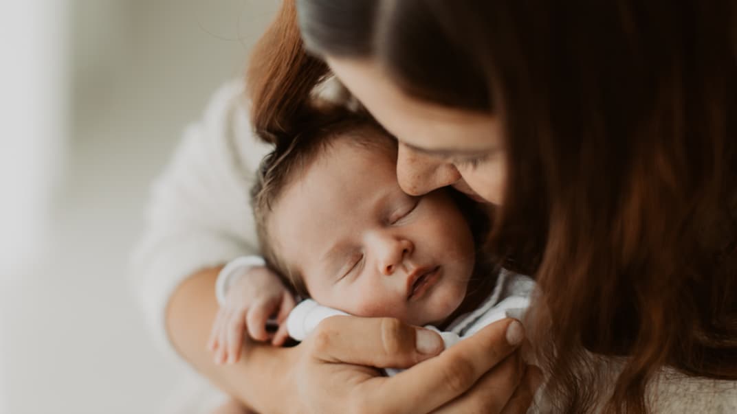 Mutter hält Neugeborenes im Arm.
