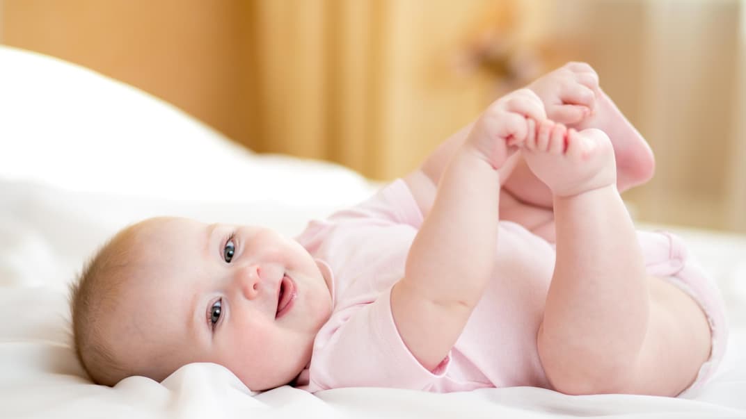 Ein kleines Baby liegt auf dem Rücken und hält sich die Füße.