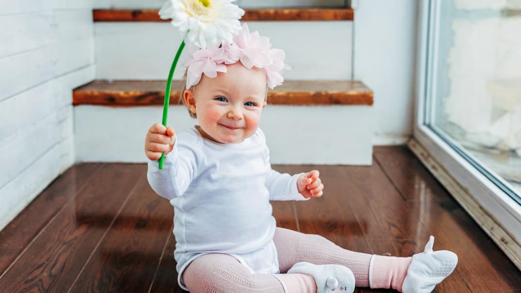 Ein kleines Mädchen lacht und hält eine Blume in der Hand. 