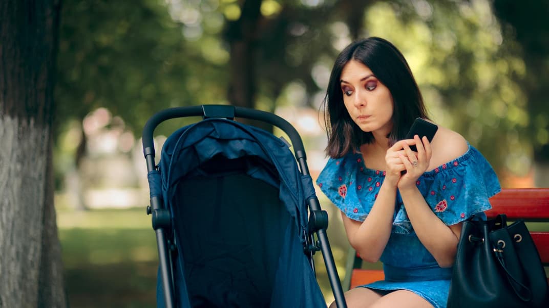 Frau sitzt mit Handy in der Hand neben dem Kinderwagen