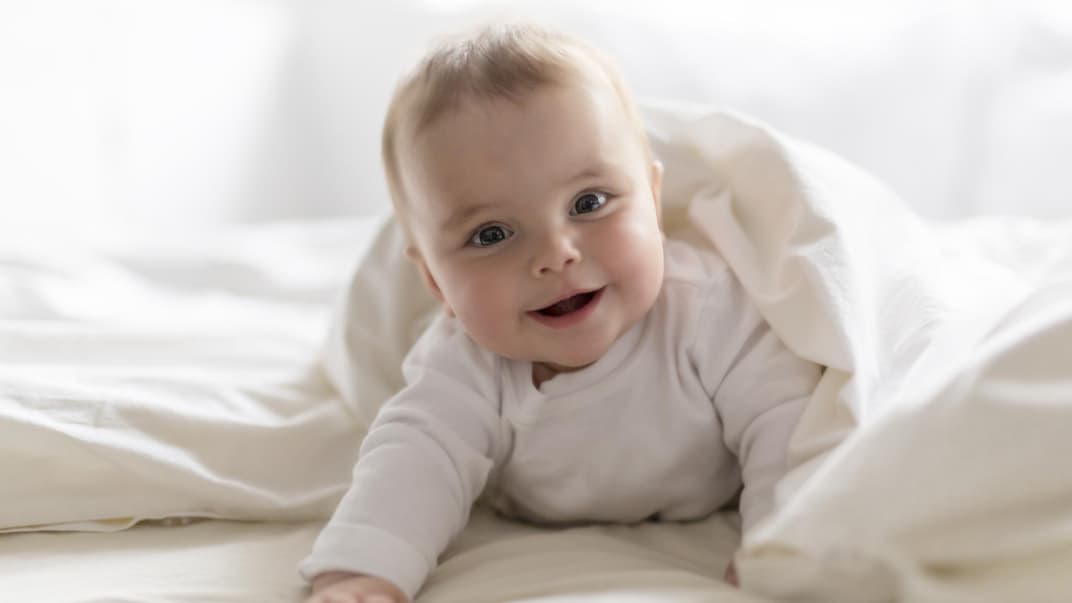 Ein Baby liegt lächelnd im Bett.