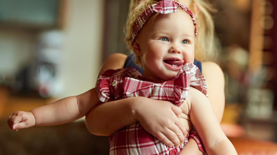 Ein kleines Mädchen lächelt in den Armen der Mutter.