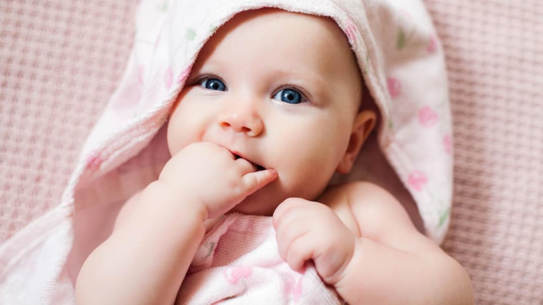 Ein kleines Baby liegt in rosa Bademantel auf einem Tuch.