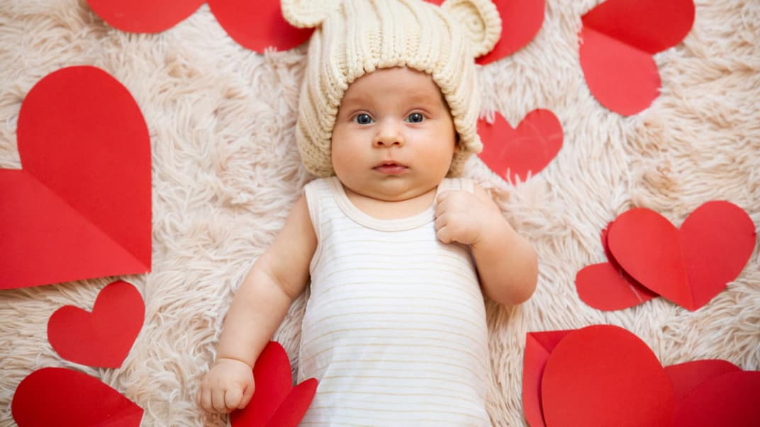 Ein Baby liegt umringt von Papierherzen auf einem Teppich.