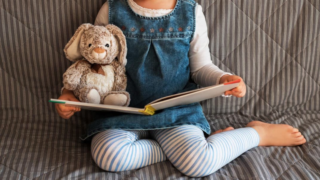 Mädchen liest zusammen mit Kuscheltier ein Kinderbuch