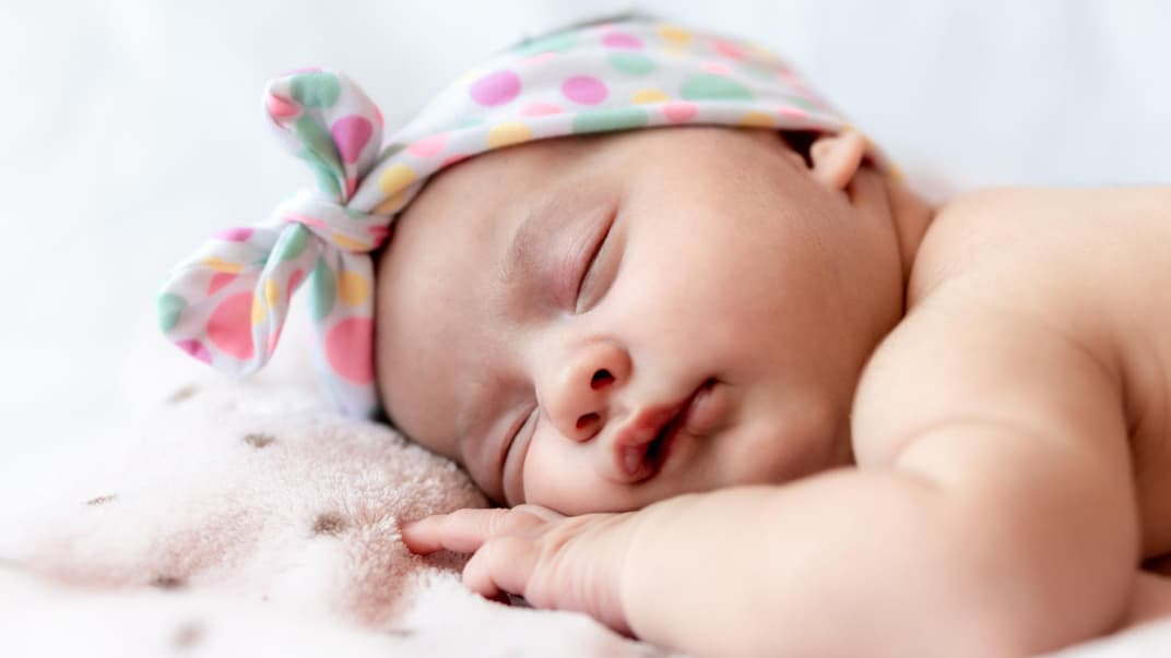 Ein Baby liegt schlafend auf dem Bauch.