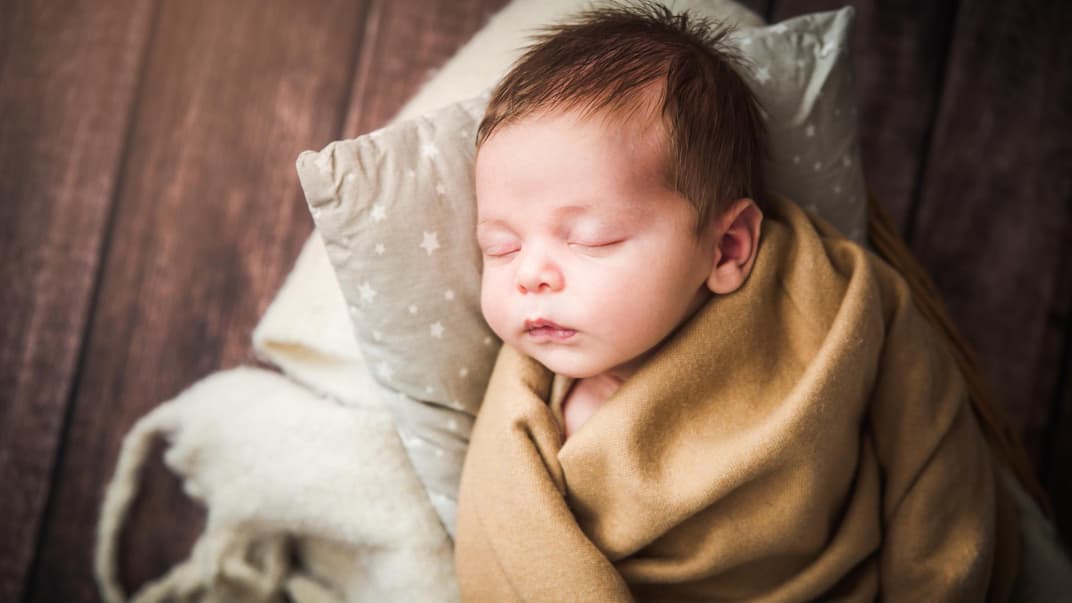 Ein Baby liegt in Decken eingewickelt und schläft.