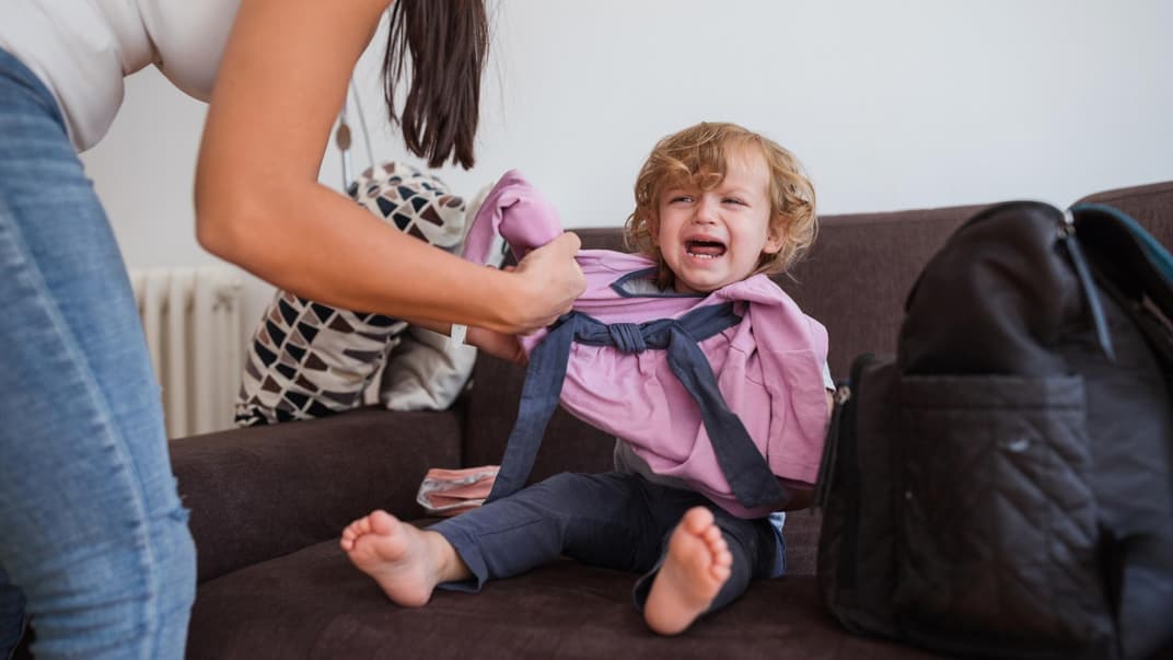 Mutter zieht weinendes Kind an.