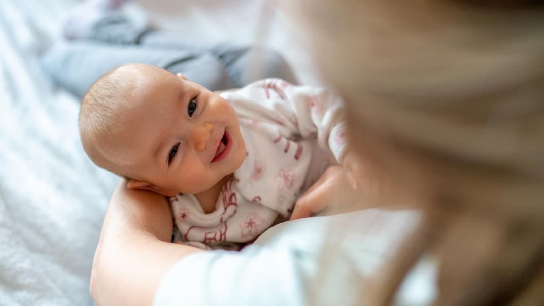 Ein Baby liegt lachend in Mamas Armen.