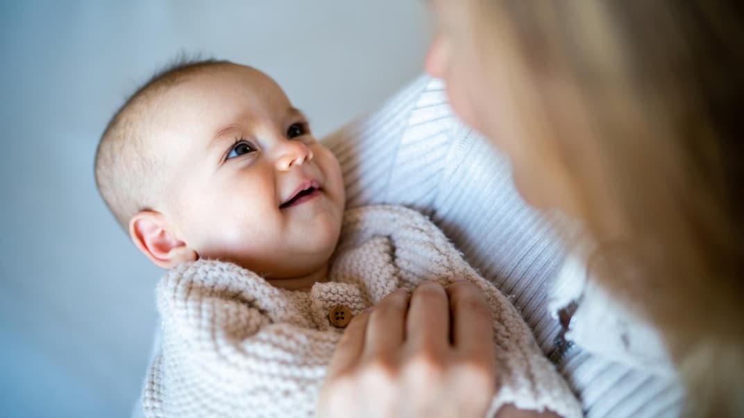 Eine Mutter hat ihr Baby auf dem Arm und es lächelt.