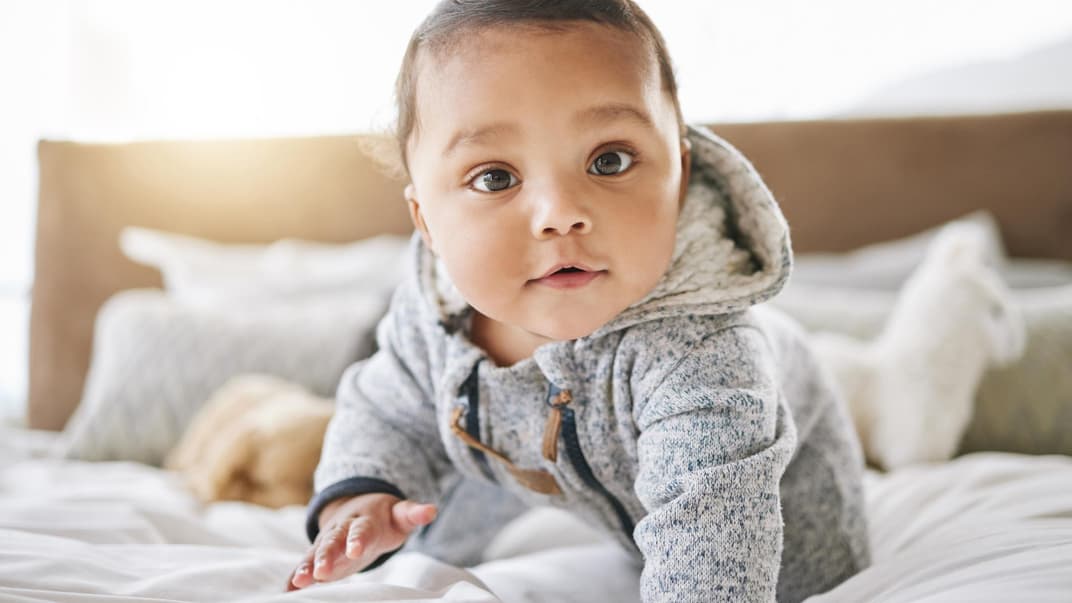 Ein kleiner Junge krabbelt auf dem Bett.