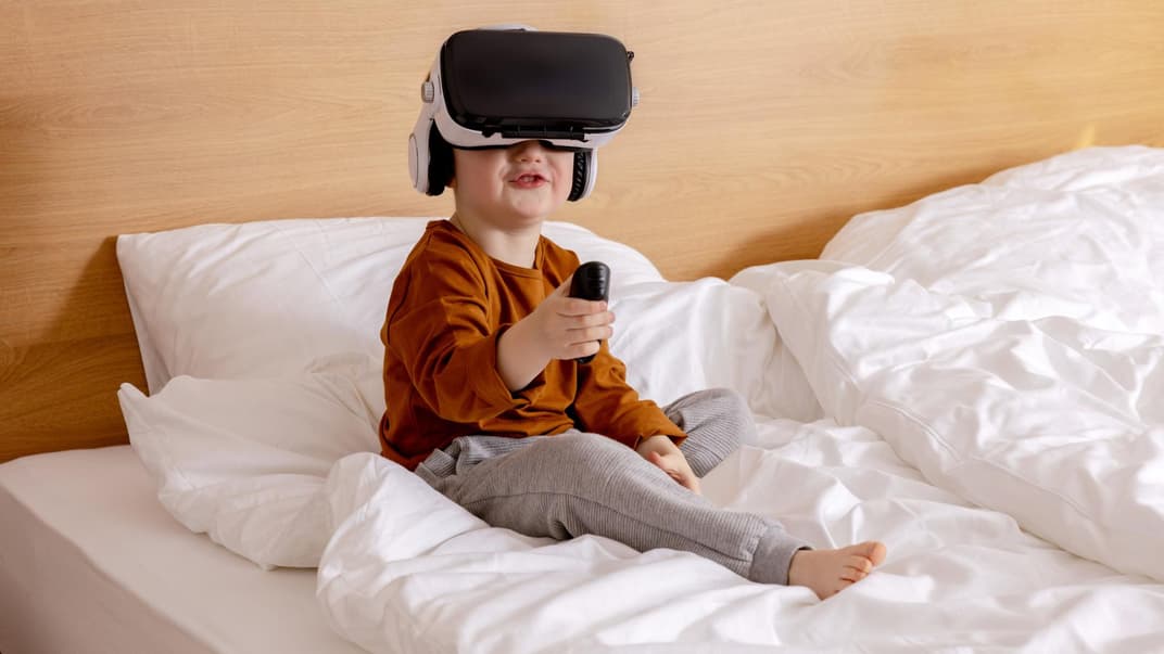 Ein kleiner Junge sitzt auf dem Bett und hat eine VR-Brille auf.
