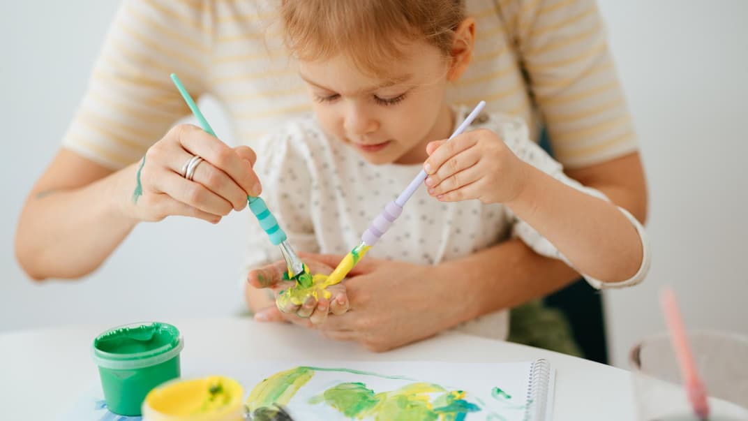 Mädchen bastelt zusammen mit ihrer Mutter ein Bild mit Handabdruck