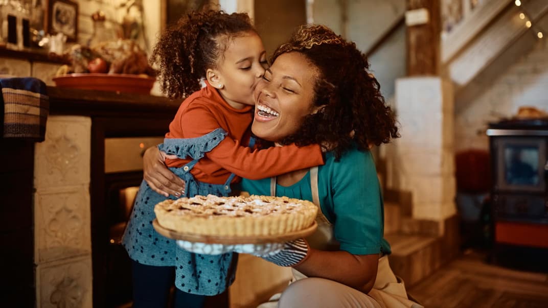 Eine Mutter hält einen Kuchen in der Hand und bekommt einen Wangenkuss von ihrer Tochter.