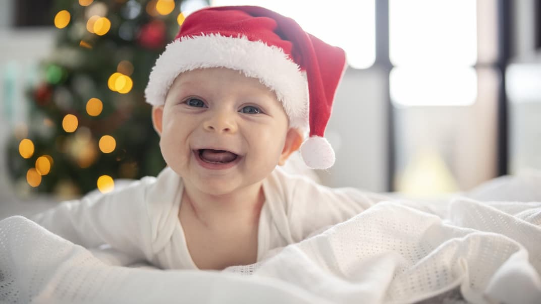 Ein Baby hat eine Weihnachtsmütze auf und lacht.