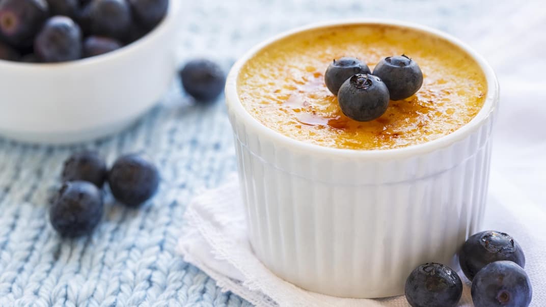 Eine Crème brulée steht auf dem Tisch und ist mit Blaubeeren garniert.