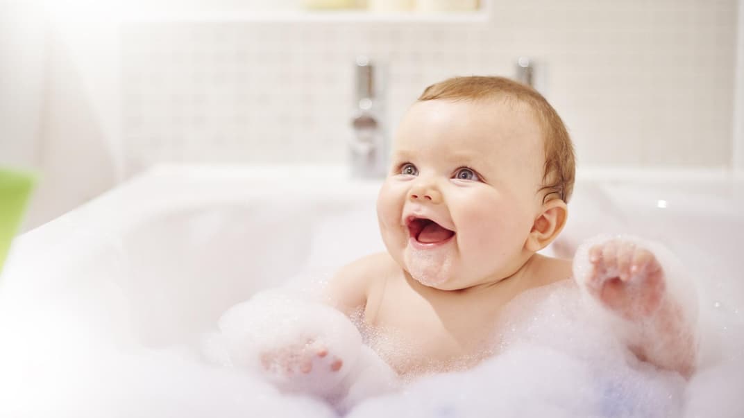 Baby sitzt in der Badewanne mit viel Schaum