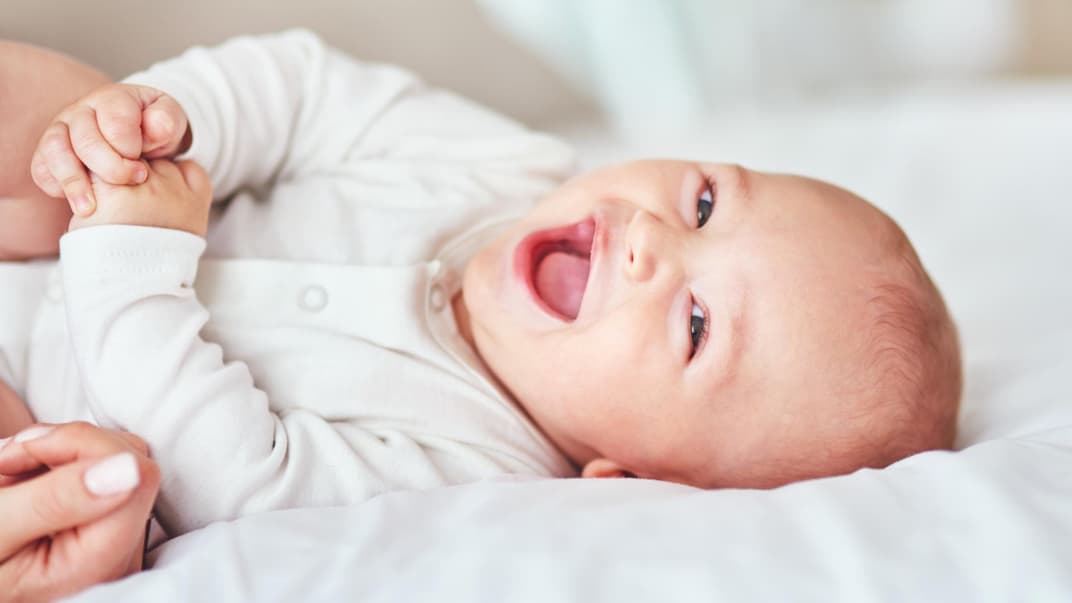 Ein kleines Baby liegt lachend auf dem Bett.