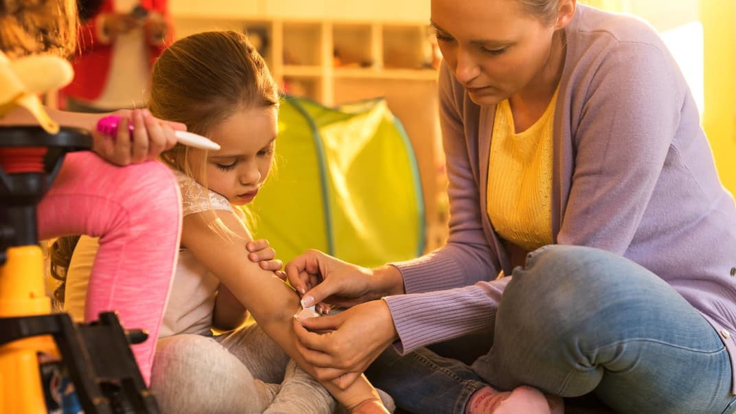 Mädchen bekommt von der Mutter ein Pflaster auf ihren Ellenbogen geklebt