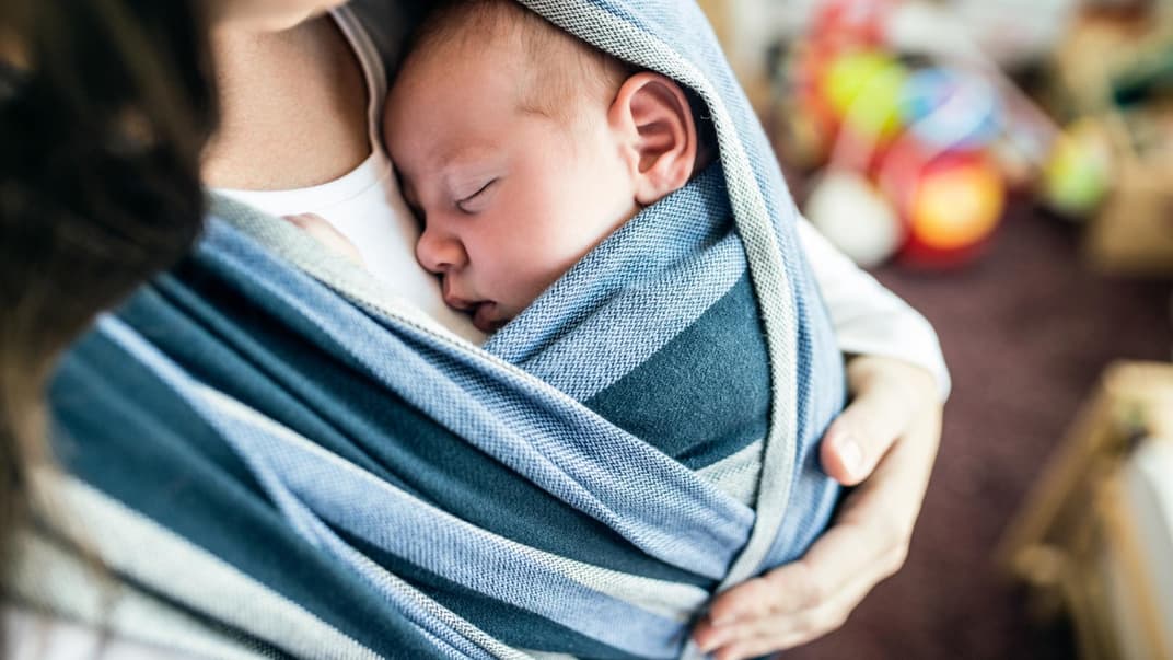 Baby im Tragetuch vor der Brust seiner Mutter.