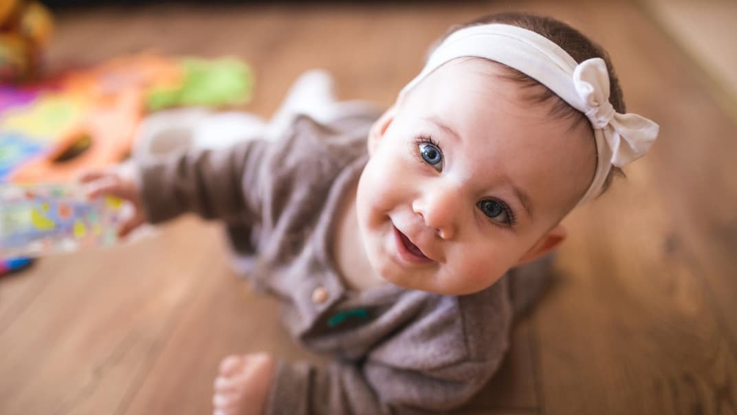Ein Baby krabbelt neben Spielsachen auf dem Boden.