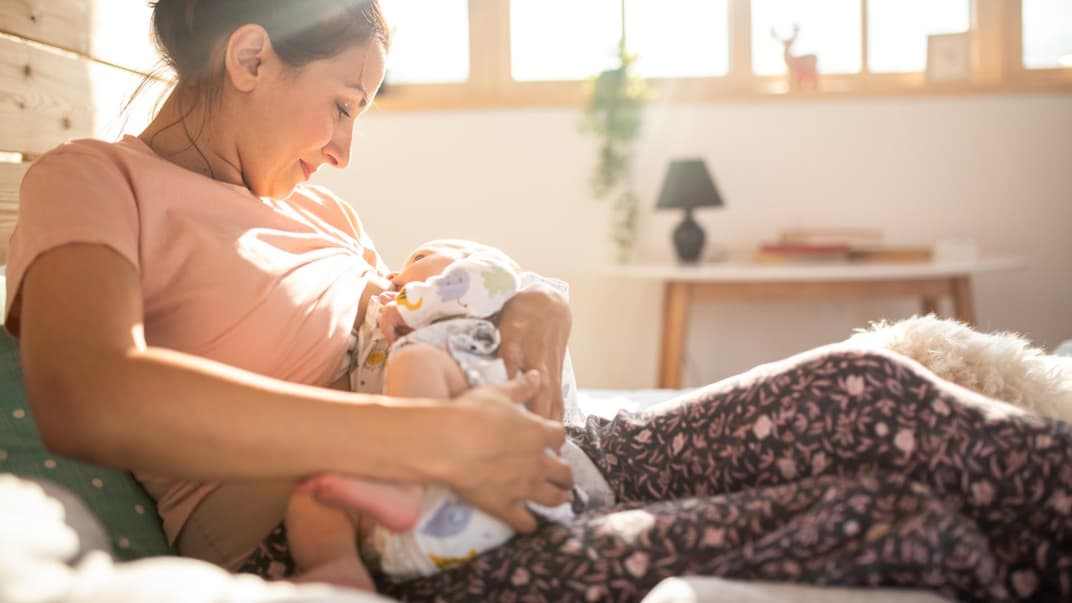 Dauernuckeln: Junge Mutter hält ihr Baby in den Armen zum Stillen und Nuckeln.