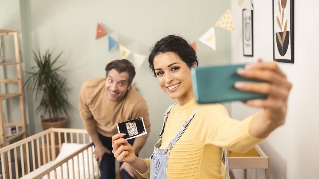 Junges Pärchen macht mit Ultraschallbild ein Selfie.