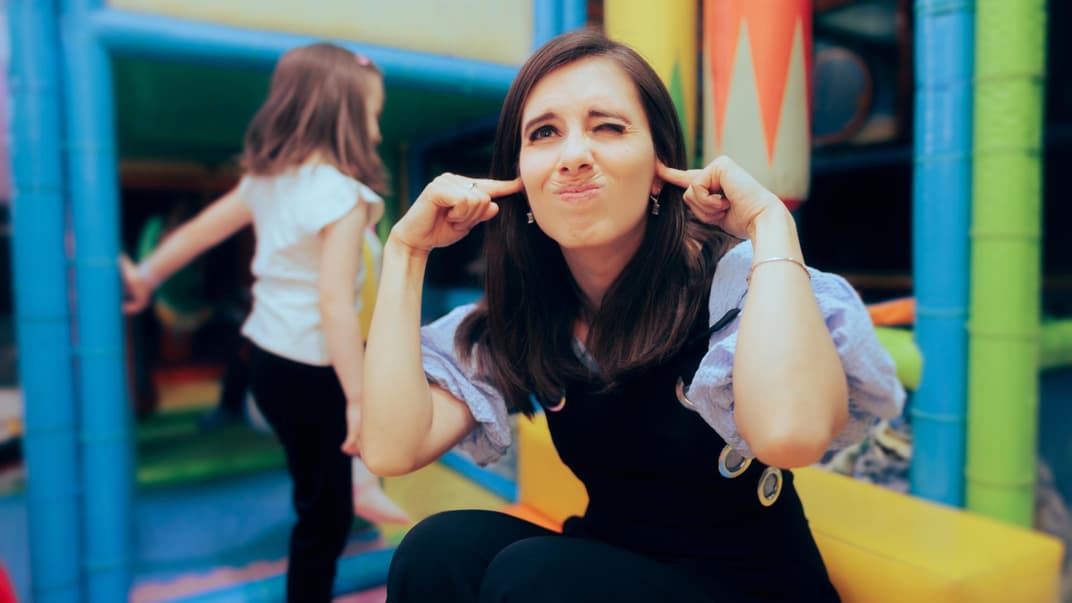 Frau hält sich auf einem Spielplatz die Ohren zu