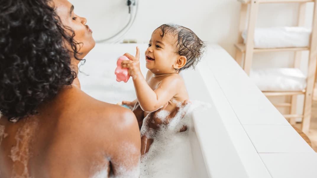 Eine Mutter badet mit ihrem Baby zusammen in der Badewanne. 