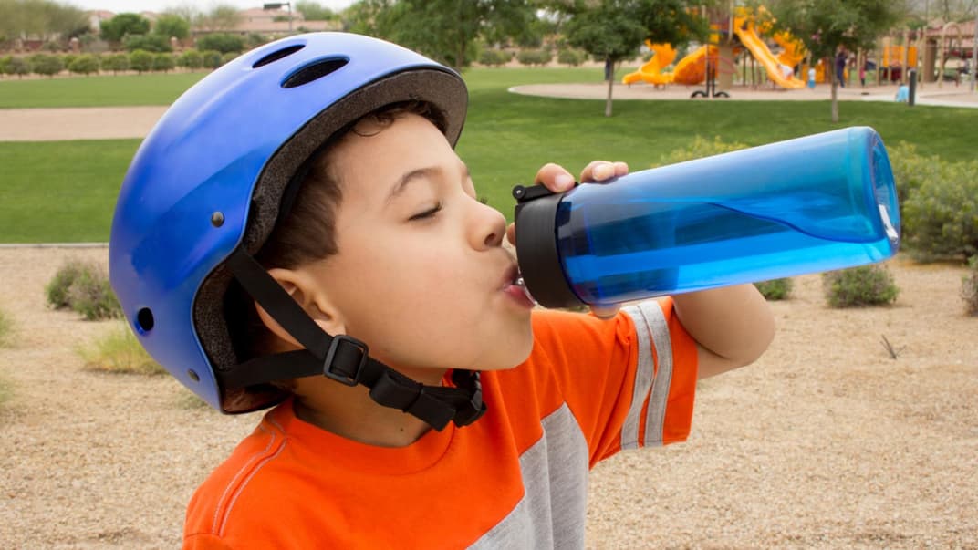 Junge trinkt im Freien aus seiner blauen Trinkflasche – doch wie reinigt man die am besten?