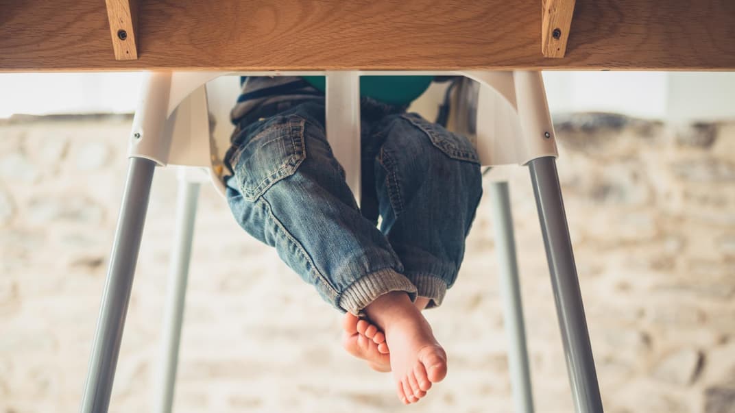 Kinderbeine unterm Tisch im Hochstuhl