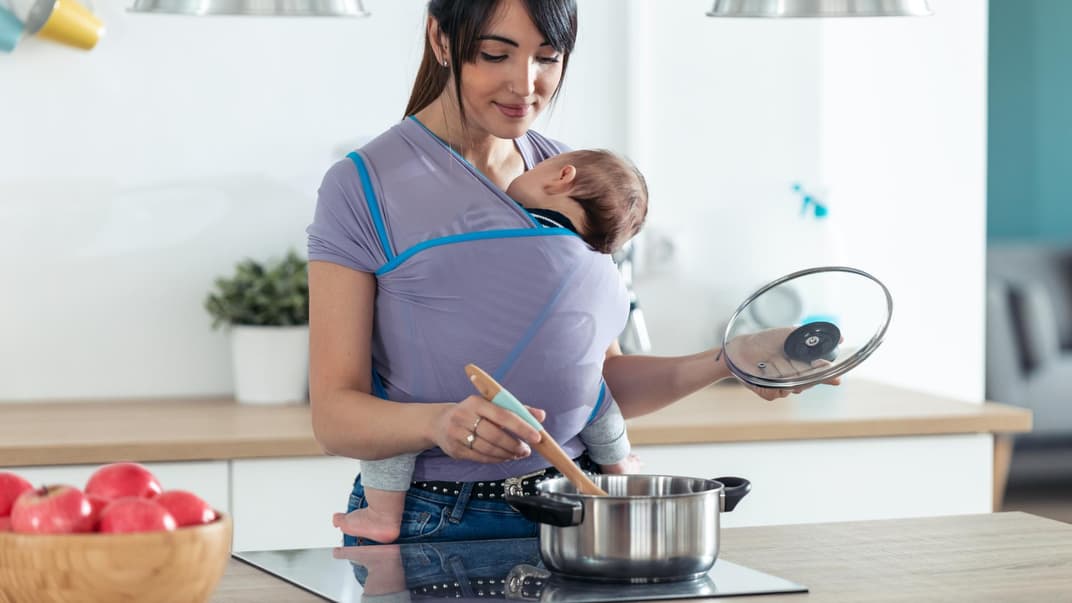 Mama mit Baby in Babytrage beim Kochen Mama mit Baby in Babytrage beim Kochen